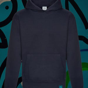 Könnte beinhalten: Ein marineblauer Kapuzenpullover mit einer Vordertasche und einer Kapuze. Der Hoodie hat ein kleines, kreisförmiges Etikett auf der Kapuze und ein weiteres unten. Der Hintergrund ist türkis mit abstrakten schwarzen und weißen Formen.