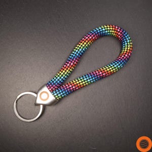 May include: A rainbow colored key chain with a silver key ring. The key chain is made of braided rope with a checkered pattern.