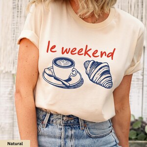 a woman wearing a t - shirt that says le weekend with a cup of coffee