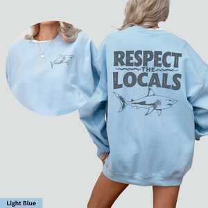 a woman wearing a light blue sweatshirt that says respect the locals