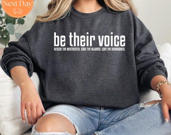 Könnte beinhalten: Dunkelgraues Sweatshirt mit dem weißen Text "be their voice" und den Sätzen "Rescue the mistreated. Save the injured. Love the abandoned." Das Sweatshirt hat einen Rundhalsausschnitt und lange Ärmel. Das Bild zeigt auch ein Versandetikett.