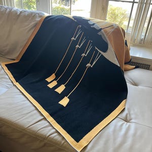 May include: A black and yellow throw blanket with a geometric design of a large black shape with five smaller yellow shapes hanging from it.