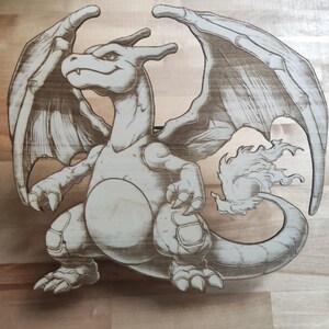 May include: A wooden carving of a dragon-like creature with large wings, a long tail with a flame, and a detailed, etched design. The artwork is in shades of brown and tan, with visible wood grain.