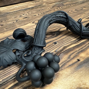 May include: Black metal grapevine design with a cluster of grapes and a leaf. The design is made to look like a vine with a branch and grapes.