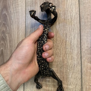May include: A bronze door handle shaped like a dog with a textured surface. The dog is standing on its hind legs with its front paws raised.