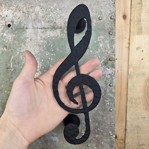 May include: Black metal door handle shaped like a treble clef. The handle has a hammered texture.