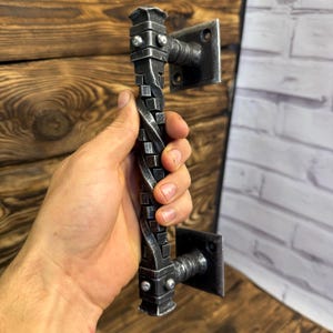 Könnte beinhalten: Ein silberner Türgriff aus Metall mit einem gedrehten Design. Der Griff ist an einer quadratischen Metallplatte befestigt.