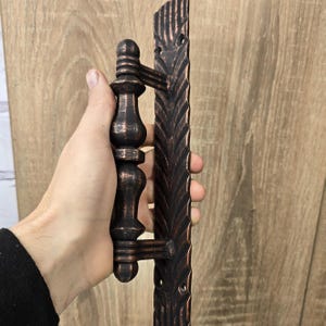 May include: A black and bronze door handle with a decorative design. The handle has a long, rectangular backplate and a round, ornate knob.