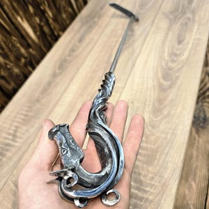 May include: A silver metal fireplace poker with a dragon head handle. The poker is twisted and has a decorative design.