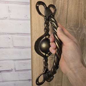 May include: A decorative door handle with a twisted rope design and a gold finish. The handle has a round orb in the center and a heart-shaped design at the top.