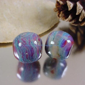 May include: Two round glass beads with a swirling pattern of blue, purple, and pink. The beads are iridescent and have a glossy finish.