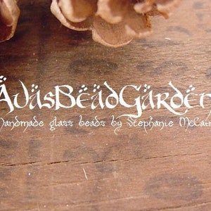May include: A white logo on a brown wooden background reads "&Auml;visBeadGarden Handmade glass beads by Stephanie McCain".