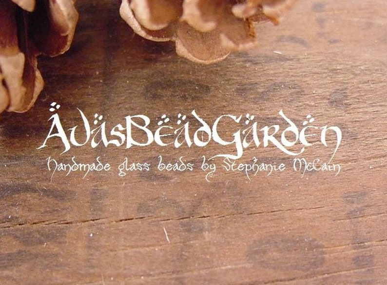 May include: A white logo on a brown wooden background reads "&Auml;visBeadGarden Handmade glass beads by Stephanie McCain".