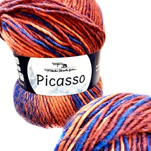 Może przedstawiać: Zbliżenie na dwie motki przędzy. Przędza jest mieszanką pomarańczowego, brązowego i niebieskiego. Etykieta głosi "Picasso" i "Filati Bertagna". Przędza jest ciasno zwinięta, idealna do robótek na drutach lub szydełku.