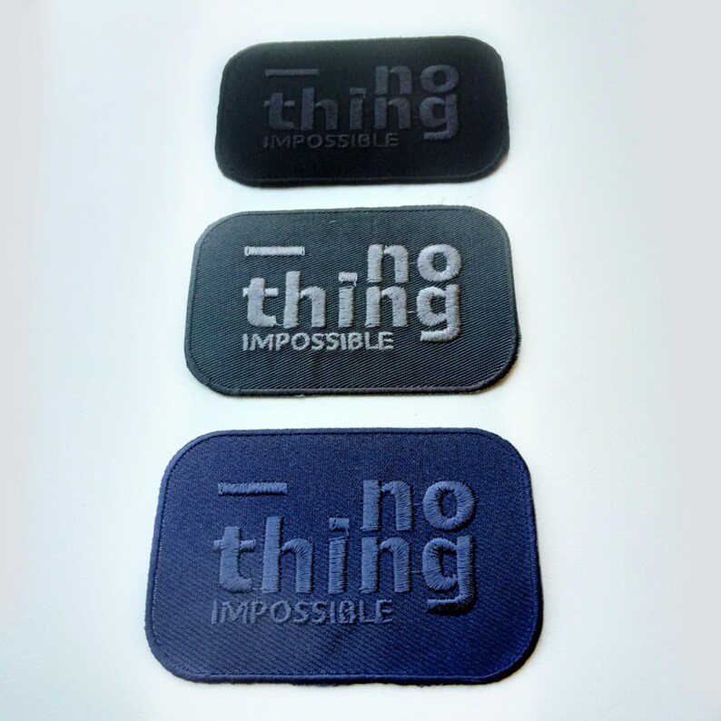 May include: Three rectangular patches with rounded corners. Each patch has the words "no thing IMPOSSIBLE" embroidered on it. The patches are black, gray, and navy blue.