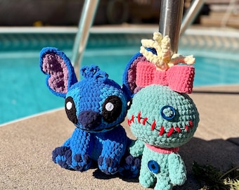May include: Two handmade crochet plush toys. One is a blue creature with large ears, black eyes, and a dark blue nose. The other is a light green doll with a pink bow, a red stitched mouth, and blue button eyes, featuring a small yellow tuft on top.