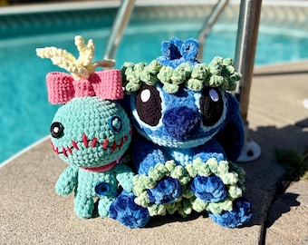 May include: Two crochet plush toys: a light blue doll with a pink bow, yellow hair, and stitched mouth, and a blue alien character wearing a green leafy lei and headpiece. Both figures feature button eyes and soft, textured yarn construction.