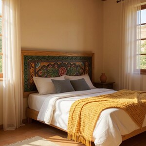 May include: A wooden bed frame with a headboard featuring a colorful floral design. The bed is made with white linens, gray pillows, and a yellow textured throw blanket. The room has a warm, inviting atmosphere with natural light.