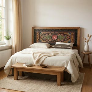 May include: A bedroom scene featuring a wooden bed frame with an ornate, carved headboard. The headboard is decorated with floral and leaf motifs in shades of red, green, and brown. The bed is made with white linens and a cream-colored throw.