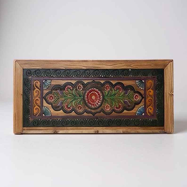 May include: A rectangular wooden box with a hand-painted floral design. The central motif features a red flower surrounded by green leaves and smaller red flowers. The border is dark green and purple, with a natural wood frame.