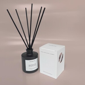 May include: A matte black glass reed diffuser bottle with six black reeds and a white label reading HALOSISTR REMAIN soft traces left behind. Beside it sits a white rectangular box with the text HALOSISTR and EVERY SCENT HOLDS A MOMENT.