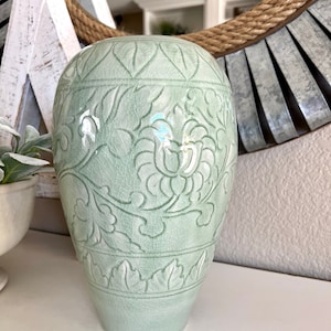 May include: A light green ceramic vase with a floral design. The vase has a crackled glaze and a rounded body.
