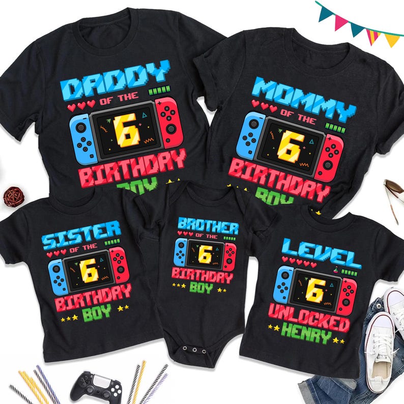 May include: Black t-shirts with video game-themed graphics. The shirts say "Daddy," "Mommy," "Sister," "Brother," and "Level Unlocked Henry." Each shirt features a pixelated game controller design with the number "6" in the center, celebrating a birthday.