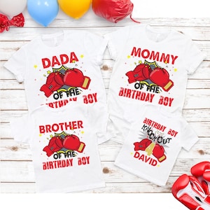May include: Four white t-shirts with red and yellow graphics. The shirts read "DADA", "MOMMY", and "BROTHER" with boxing glove illustrations. The fourth shirt says "BIRTHDAY BOY Knock Out" and "DAVID".