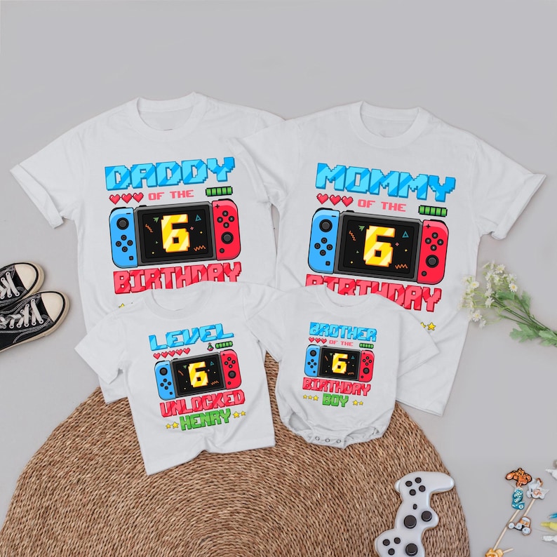May include: White t-shirts and a onesie with a video game controller design. The shirts read "Daddy," "Mommy," "Level Unlocked Henry," and "Brother." Each shirt features a number 6, and the word "Birthday."