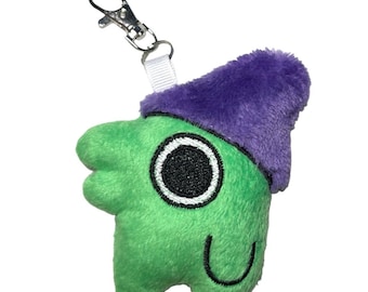 May include: A plush green creature keychain with a purple hat and a silver metal clasp. The creature has a smiling face with a black eye and a white outline. The keychain is made of soft, fuzzy material.