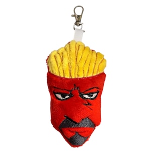 May include: A plush keychain featuring a red anthropomorphic french fry character with an angry expression. The character has yellow fries on top, black eyebrows, and a black mustache and mouth. It includes a metal clasp and white fabric loop.