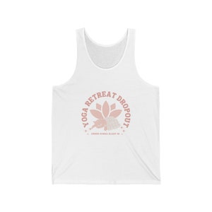 May include: White tank top with a pink graphic. The graphic reads "YOGA RETREAT DROPOUT" in a circle around a lotus flower and a sleeping animal. Below the animal, the text reads "OMMM GONNA SLEEP IN +"