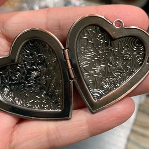 K&ouml;nnte beinhalten: Ein herzf&ouml;rmiges Medaillon mit einem detaillierten Blumenmuster auf beiden Seiten. Das Medaillon ist aus Metall mit einer kupfernen Oberfl&auml;che.
