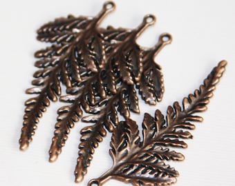 May include: Five antique copper fern charms with a loop at the top for hanging. The charms are detailed with intricate fern leaf designs.