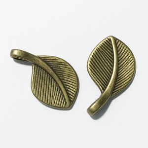 May include: Two antique gold leaf charms with a detailed vein pattern. The charms are made of metal and have a loop for attaching to jewelry or other crafts.