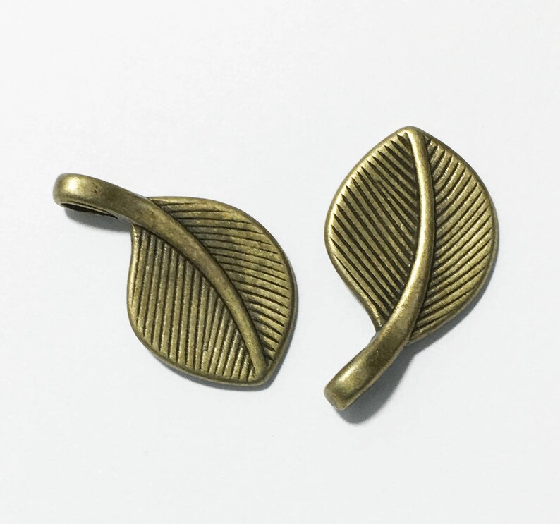 May include: Two antique gold leaf charms with a detailed vein pattern. The charms are made of metal and have a loop for attaching to jewelry or other crafts.