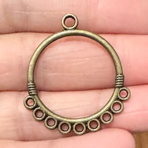 May include: A bronze-colored metal pendant with a circular frame and a smaller circle at the top for hanging. The frame has a decorative row of smaller circles around the bottom.