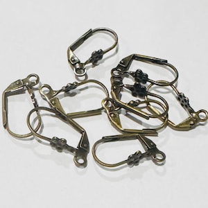 May include: A collection of antique brass-colored earring findings, including lever-back and French hook styles. Each finding features a decorative floral accent. The findings are scattered on a white surface.