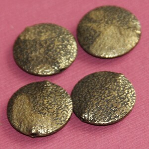 May include: Four round, gold-colored, textured beads with a hole in the center.