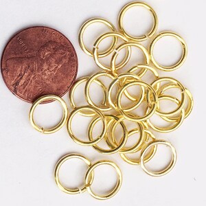 May include: A pile of gold jump rings, some are overlapping, next to a US penny. The jump rings are about the size of a penny.