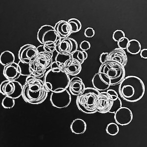 May include: A large quantity of silver jump rings of various sizes, scattered on a black background.