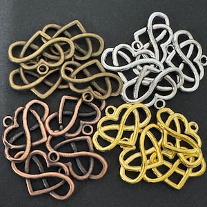 Può includere: Una collezione di ciondoli in metallo a forma di cuore infinito in quattro diverse finiture: bronzo antico, argento, rame e oro. Ogni ciondolo presenta un design intrecciato con un piccolo occhiello sulla parte superiore per l'aggancio.