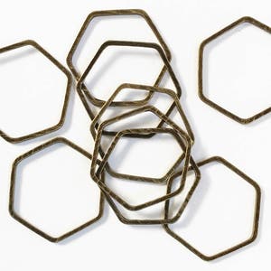 May include: A set of eight gold-toned metal hexagonal hoops of varying sizes. The hoops are arranged in a random pattern, with some overlapping.