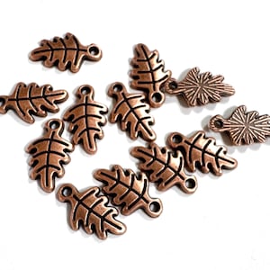 May include: A collection of twelve copper-toned metal charms shaped like oak leaves. Each charm features a detailed embossed vein pattern and a small circular loop at the top for attachment. The charms have a metallic finish with dark accents.