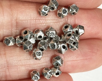 May include: A pile of silver metal beads with a geometric design. The beads have a hole in the center for stringing.