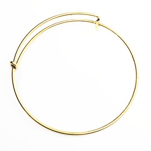 May include: A gold-toned bangle bracelet with a simple, circular design. The bracelet is made of metal and has a spring-loaded clasp.