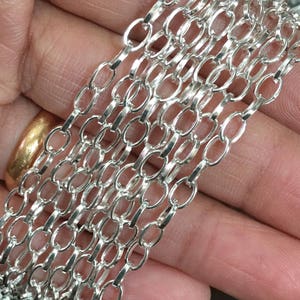 May include: Silver chain with oval links. The chain is shown in a close-up view, with multiple strands of the chain layered on top of each other.