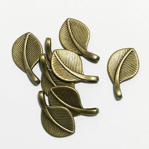 May include: A group of six antique gold leaf charms. Each charm is shaped like a leaf with a small loop at the top for attaching to jewelry or other crafts.