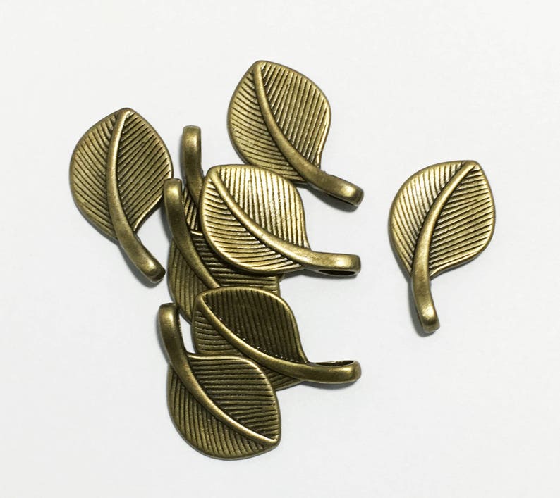 May include: A group of six antique gold leaf charms. Each charm is shaped like a leaf with a small loop at the top for attaching to jewelry or other crafts.