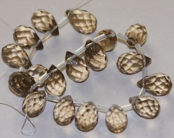 May include: A strand of faceted smoky quartz teardrop beads, strung on a clear elastic cord. The beads are a light brown color and have a faceted, teardrop shape.